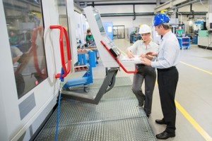 Mid-adult male manager and a female engineer programming a CNC machine at the manufacturing plant.