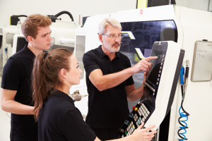 Two Apprentices Working With Engineer On CNC Machinery
